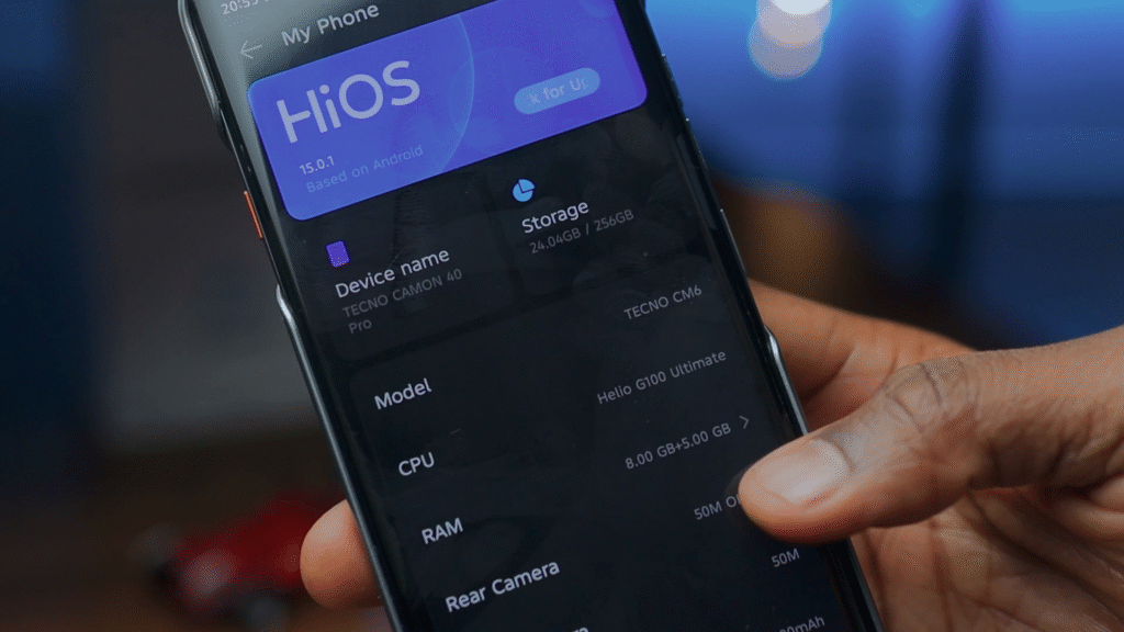 Close-up of a hand holding a smartphone displaying the HiOS version and specifications of the Tecno Camon 40 Pro, including model, CPU, RAM, and storage details.