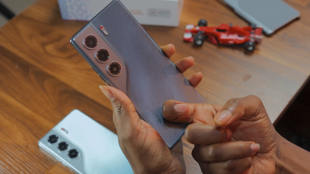 A person holding the Tecno Camon 40 Pro 4G smartphone, showcasing its sleek design and triple-camera setup, with a colorful toy car and another phone in the background.