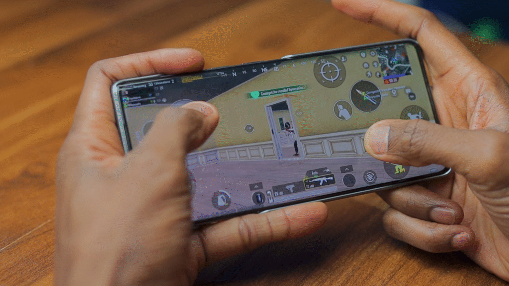 A person holding a smartphone while playing a mobile game, showing their fingers on the device's screen, with a gaming interface visible.